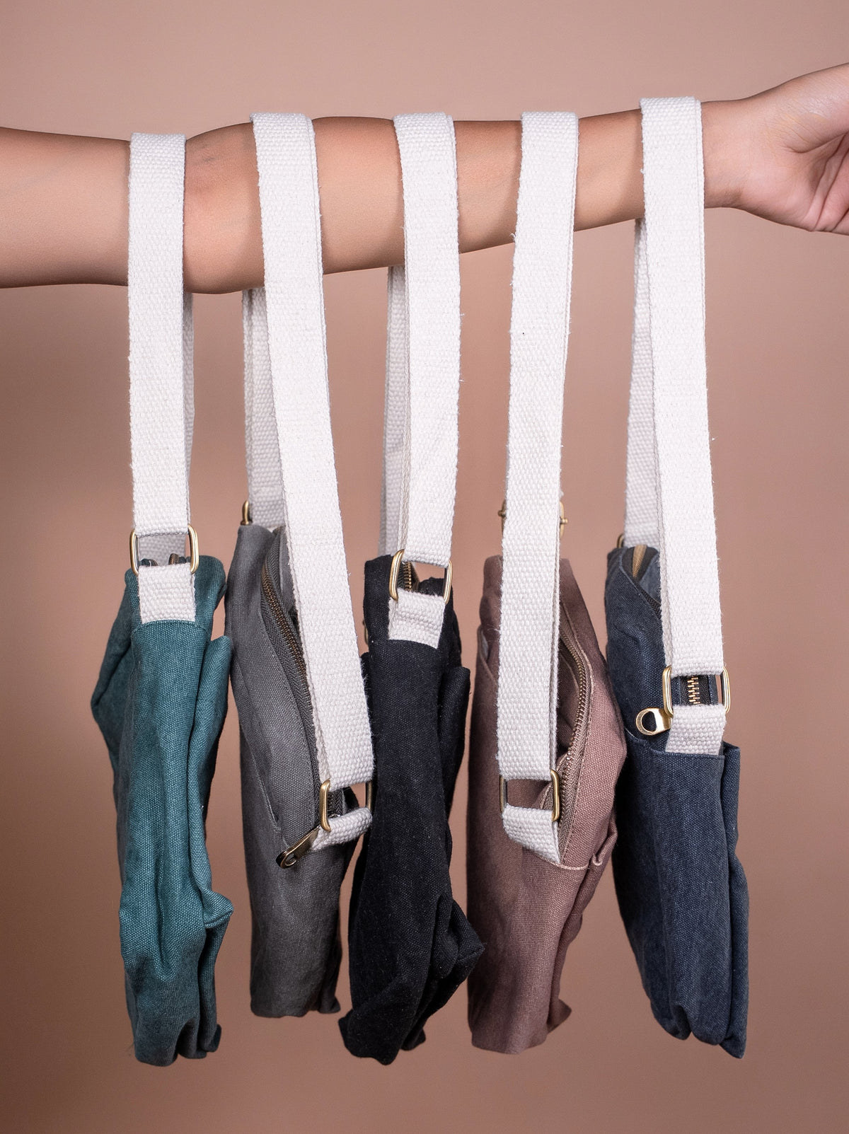 Hand showing Nava Crossbody bags in various colours